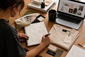 Fashion designer creating a custom clothing brand with apparel sketches, fabric swatches, and branded clothing labels.