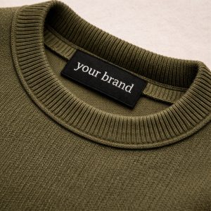 custom woven clothing label sewn into olive green sweater showing brand identity